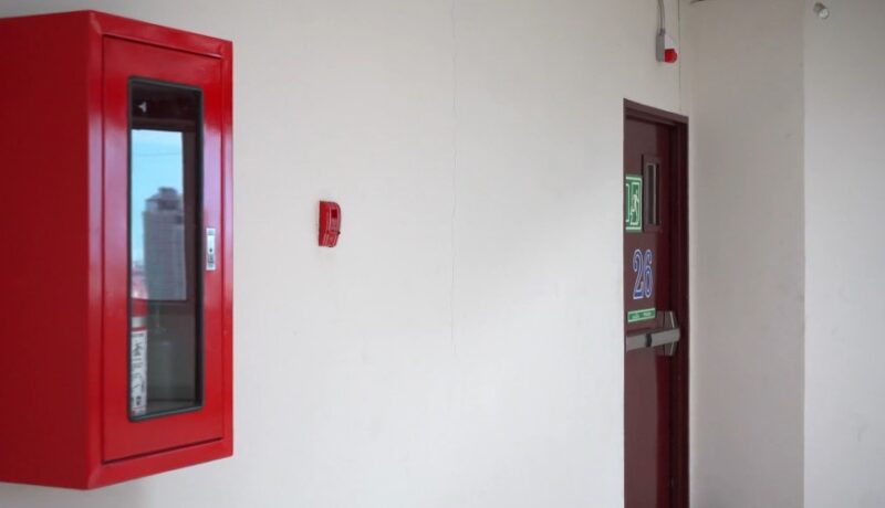A red fire safety cabinet and a fire alarm are mounted on a white wall